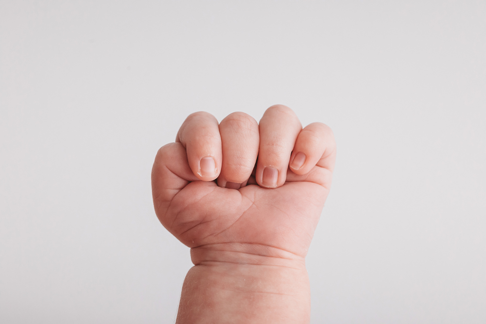 Tiny newborn hand in a soft fist against a cream backdrop by Reflection Images, Florence SC newborn photographer.