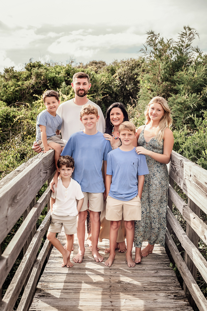 Culpepper family poses on a Pawleys Island SC wooden boardwalk wearing powder blue shirts and tan shorts for beach portraits.