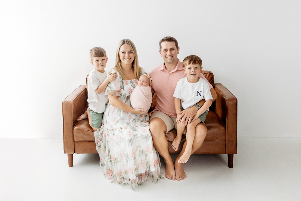 Family on cognac leather sofa, newborn in blush swaddle, by Reflection Images Florence SC newborn photographer.