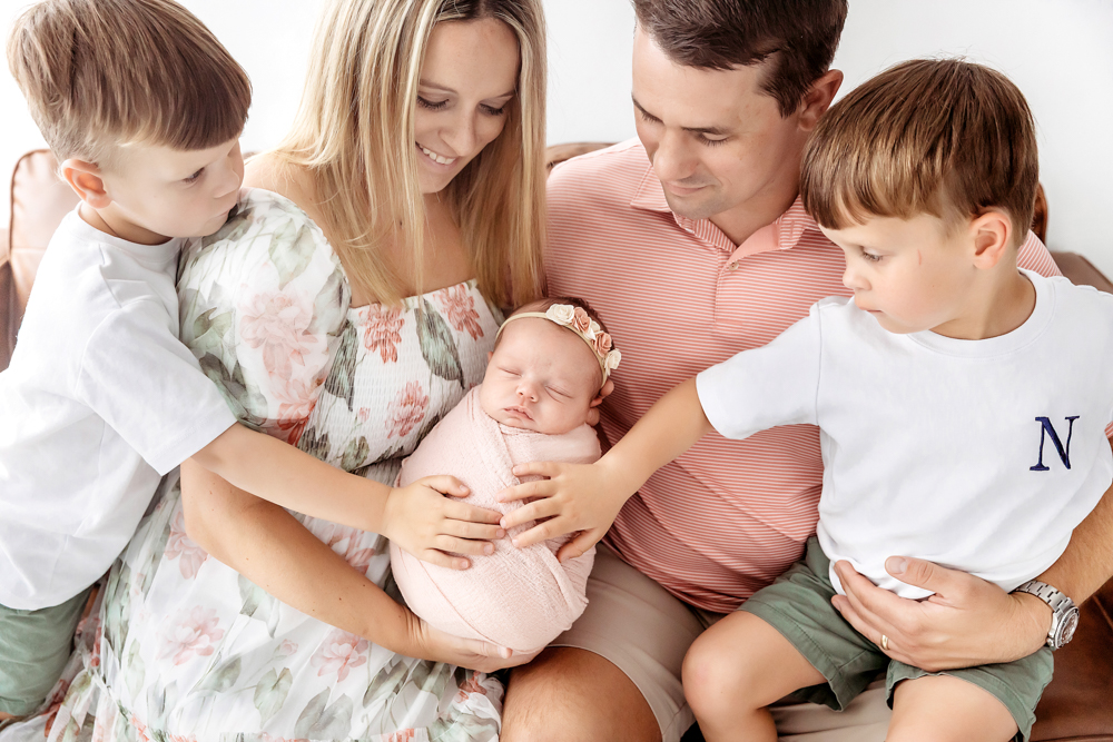 Family newborn session by Tracy Rowell in Florence SC. Parents and brothers touch baby in a blush knit swaddle.