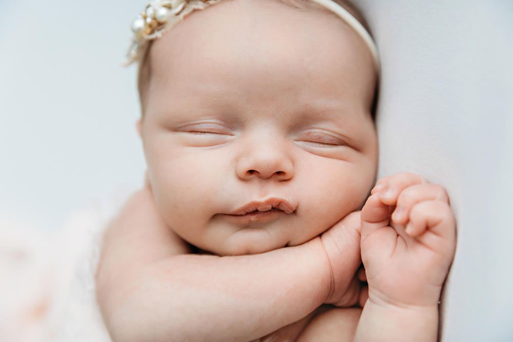 Sleeping newborn baby girl by Florence SC photographer Tracy Rowell wearing an ivory pearl headband on cream backdrop.
