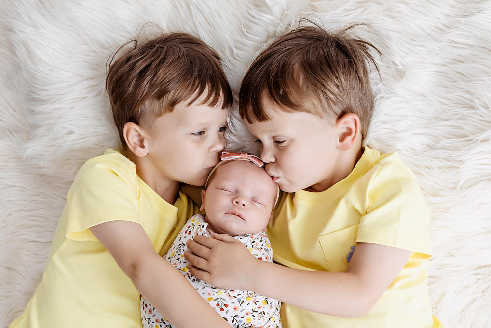 twin brothers in yellow tees kiss newborn Gracyn on white fur by Florence SC photographer Reflection Images by Tracy Rowell