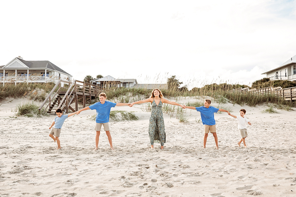 sibling poses on the beach holds hands with four brothers in blue shirts on Pawleys Island SC beach for family photography.
