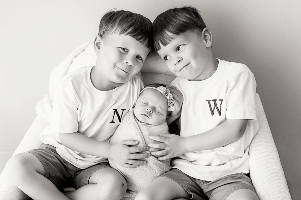 Black and white newborn sibling portrait by Tracy Rowell in Florence SC with brothers holding a swaddled baby girl.